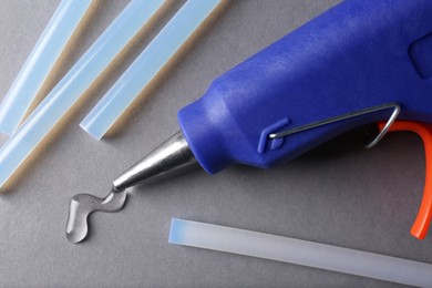 Photo of Melted glue dripping out of hot gun nozzle near sticks on grey background, closeup