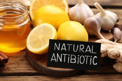 Photo of Different fresh products and card with phrase Natural Antibiotic on wooden table, closeup