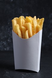 Photo of Delicious french fries in paper box on black table