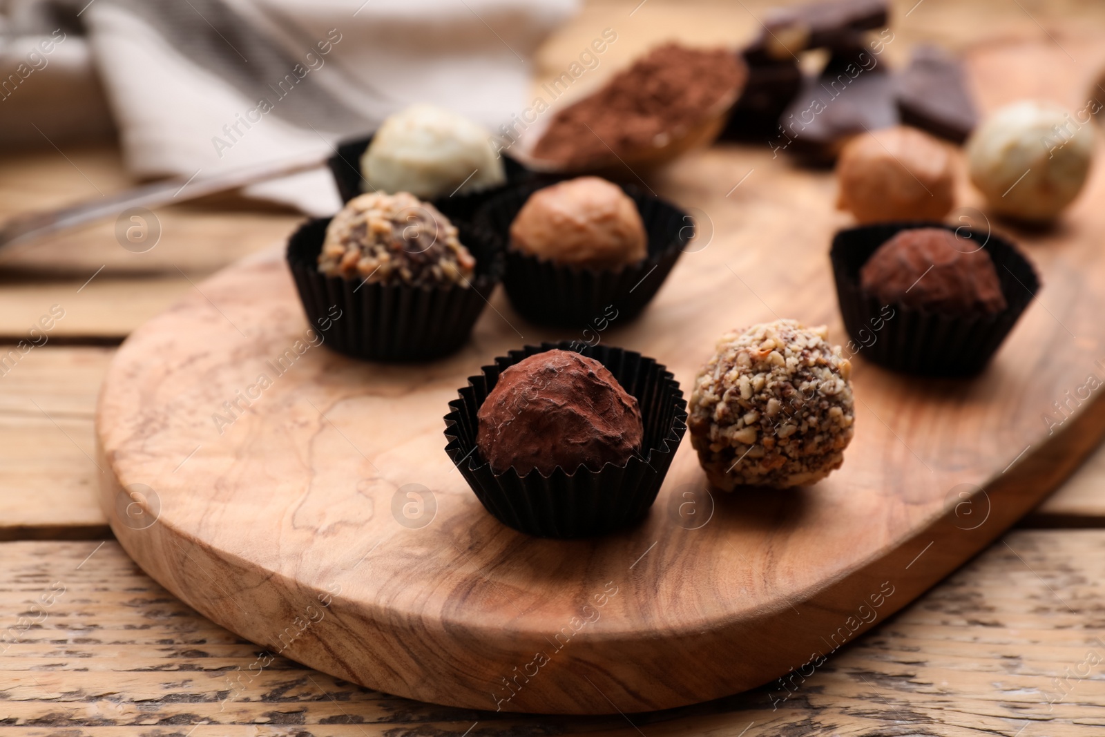 Photo of Different tasty chocolate candies on wooden board, closeup