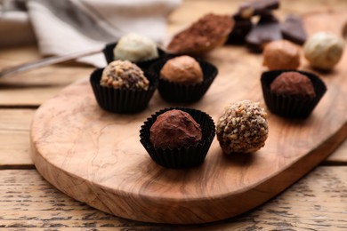 Different tasty chocolate candies on wooden board, closeup