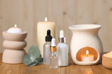 Photo of Different aromatherapy products, burning candles and eucalyptus leaves on wooden table