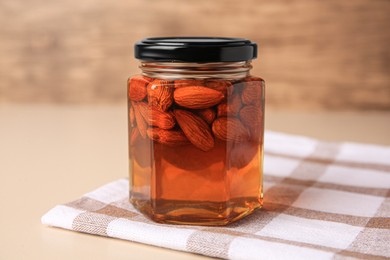 Photo of Jar with almonds and honey on beige table