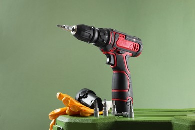Photo of Electric screwdriver, drill bits, battery and gloves on case against pale green background