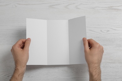 Photo of Man with blank brochure on wooden background, above view. Mock up for design