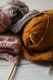 Balls of soft yarns, knitting and needles on white wooden table, closeup