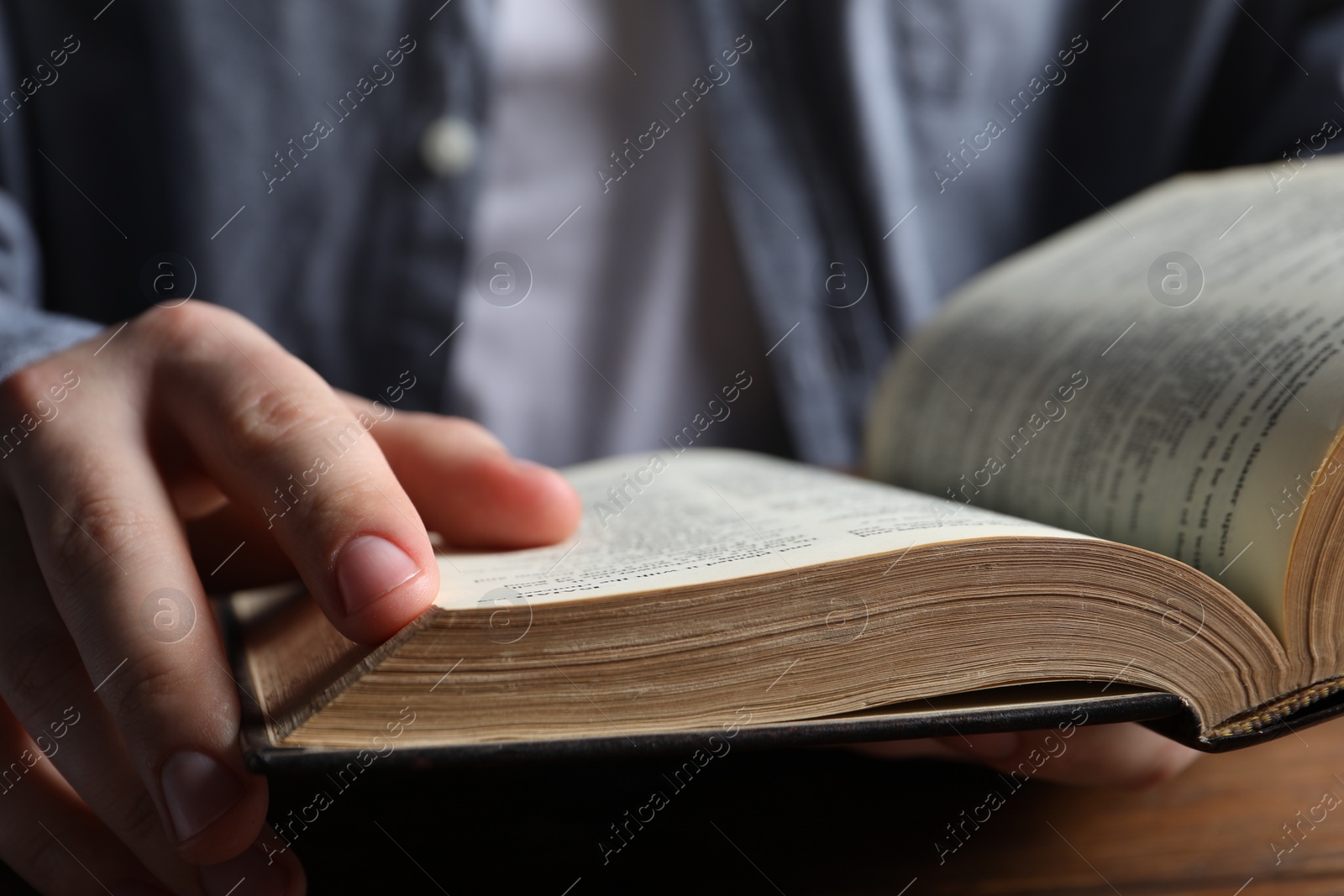 Photo of Man reading holy Bible at wooden table, closeup