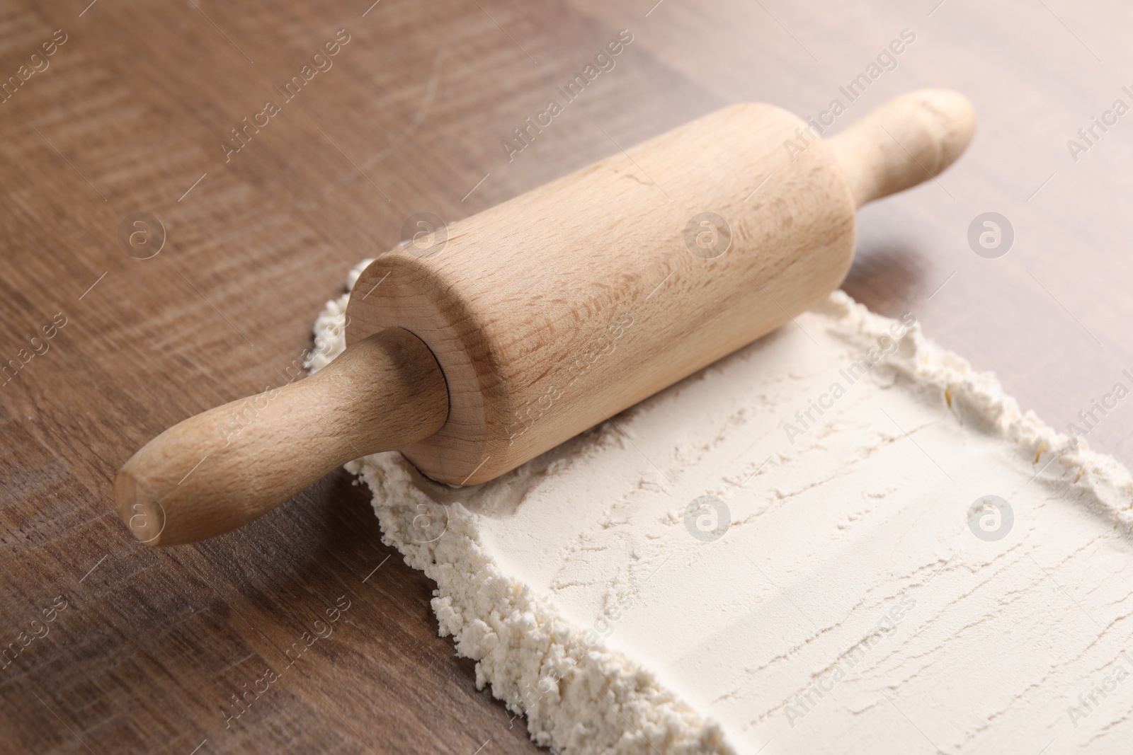 Photo of Flour and rolling pin on wooden table, closeup