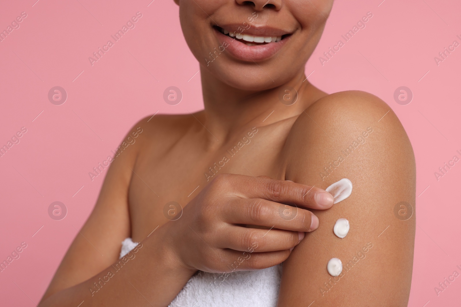 Photo of Young woman applying body cream onto arm on pink background, closeup