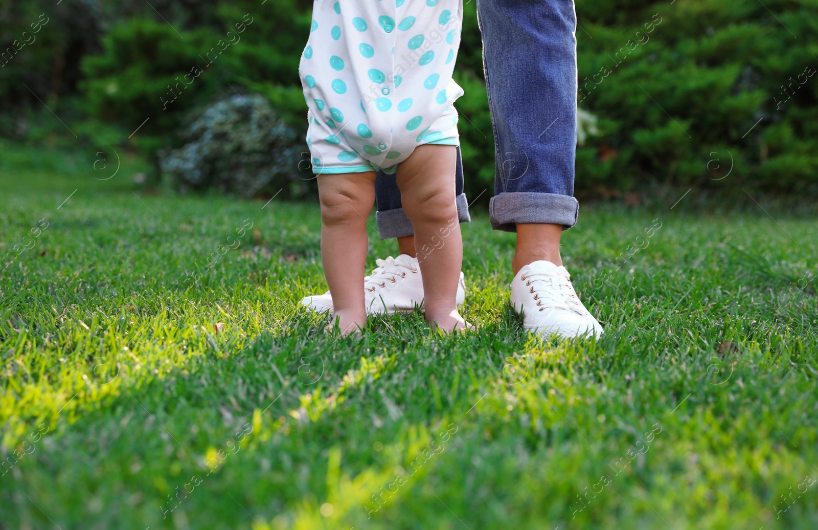 Photo of Cute little baby learning to walk with his nanny on green grass outdoors, closeup