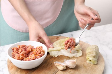 Photo of Woman preparing stuffed cabbage roll at white marble table, closeup