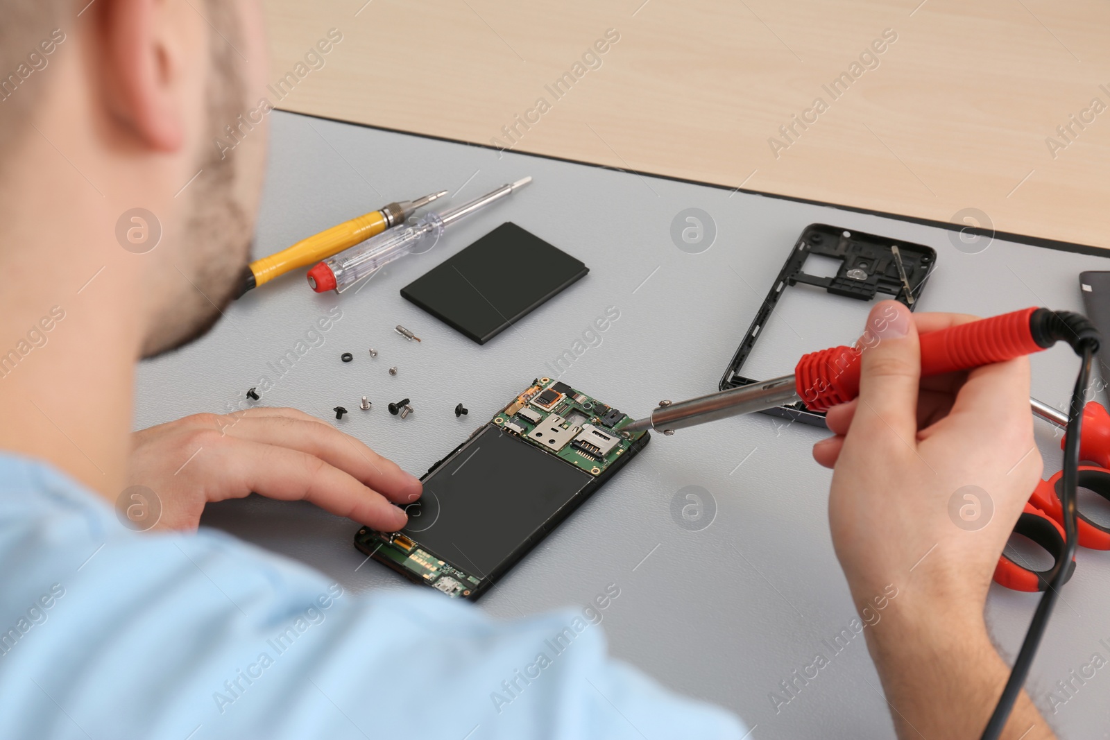 Photo of Technician repairing broken smartphone at table, closeup