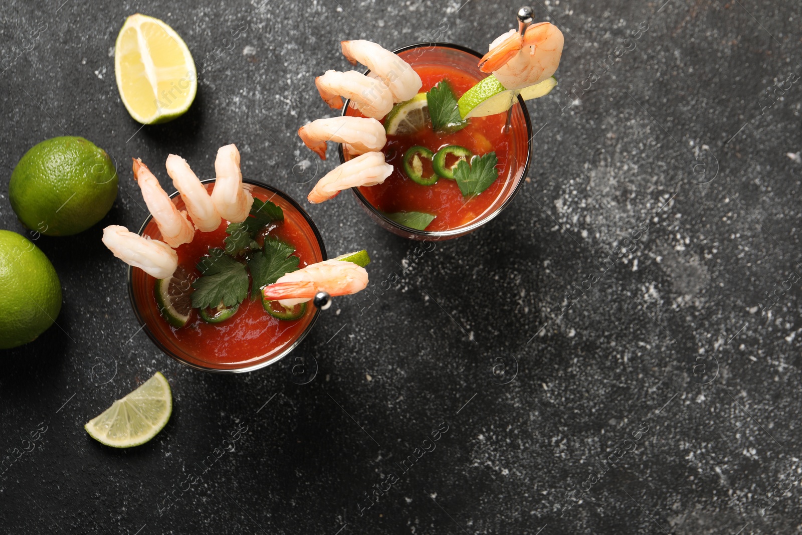 Photo of Tasty shrimp cocktail with sauce in glasses and limes on grey textured table, flat lay. Space for text