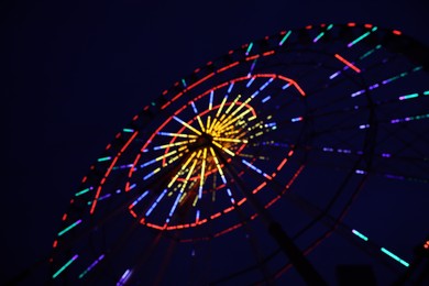 Blurred view of beautiful glowing Ferris wheel against dark sky