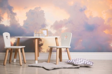 Picturesque sky with clouds as wallpaper pattern. Baby room interior with table and chairs near wall
