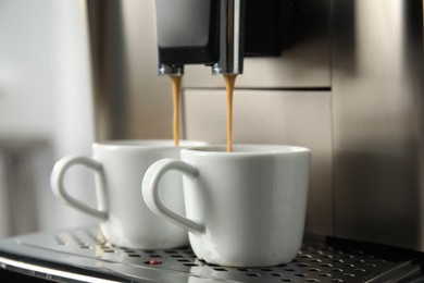 Photo of Espresso machine pouring coffee into cups against blurred background, closeup