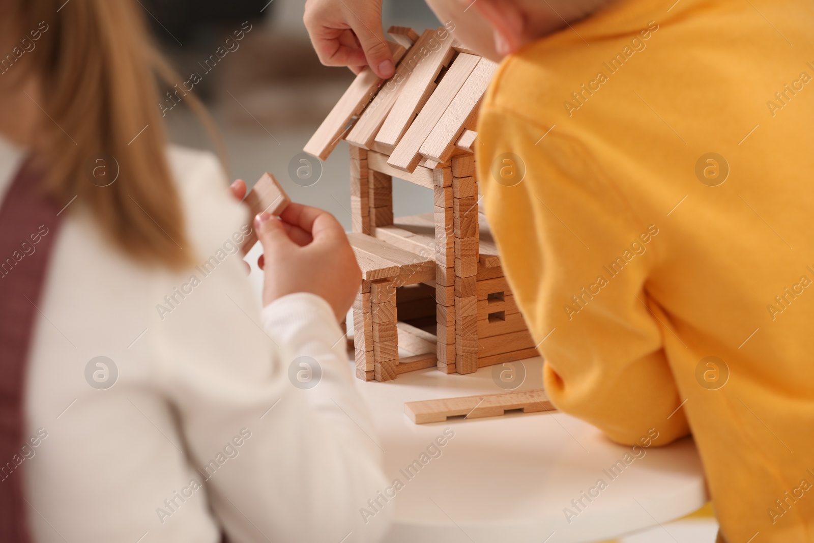 Photo of Little boy and girl playing with wooden house at white table indoors, closeup. Children's toys