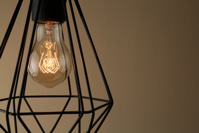 Hanging lamp bulb in chandelier against brown background, closeup. Space for text