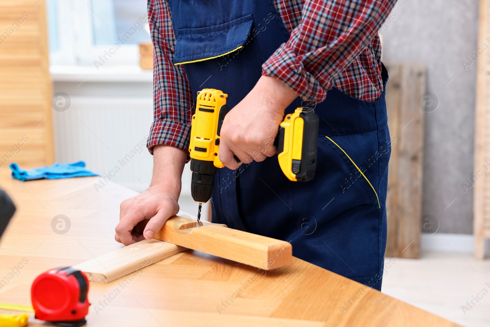 Photo of Young worker using electric drill at table in workshop, closeup