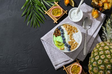 Photo of Tasty smoothie bowl with fresh kiwi fruit, blueberries and oatmeal served on black table, flat lay. Space for text