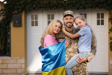 Soldier in military uniform reunited with his family and Ukrainian flag outdoors, space for text