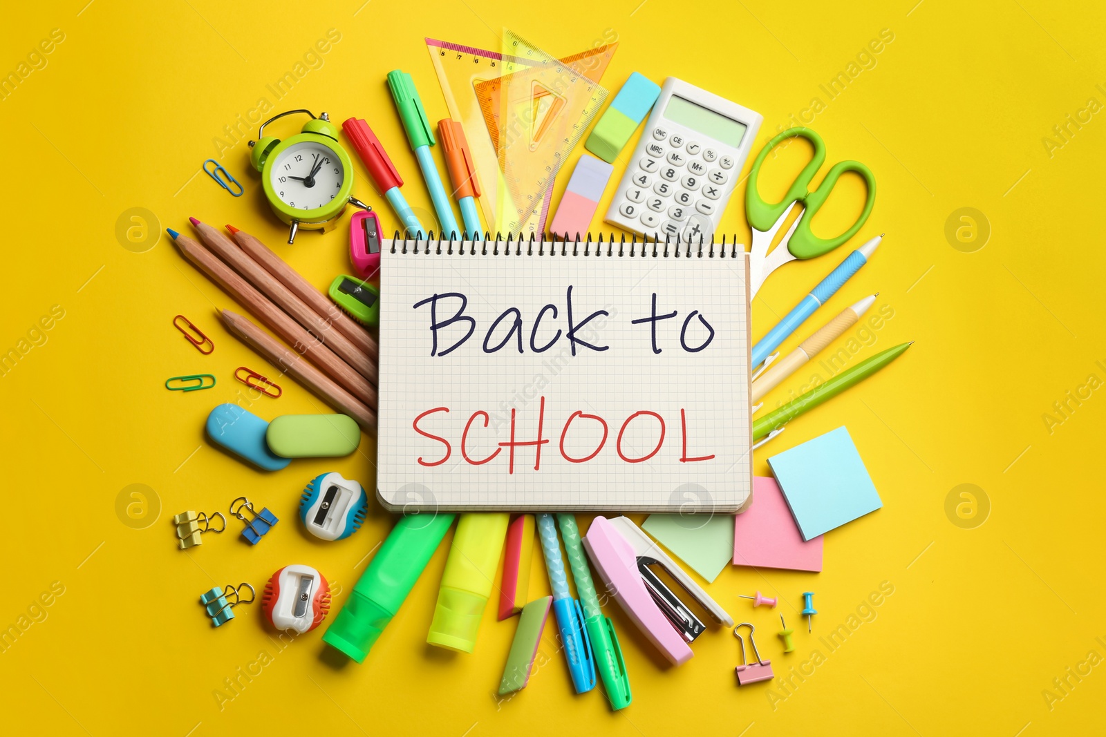 Image of Notebook with text Back To School surrounded by different stationery on yellow, flat lay