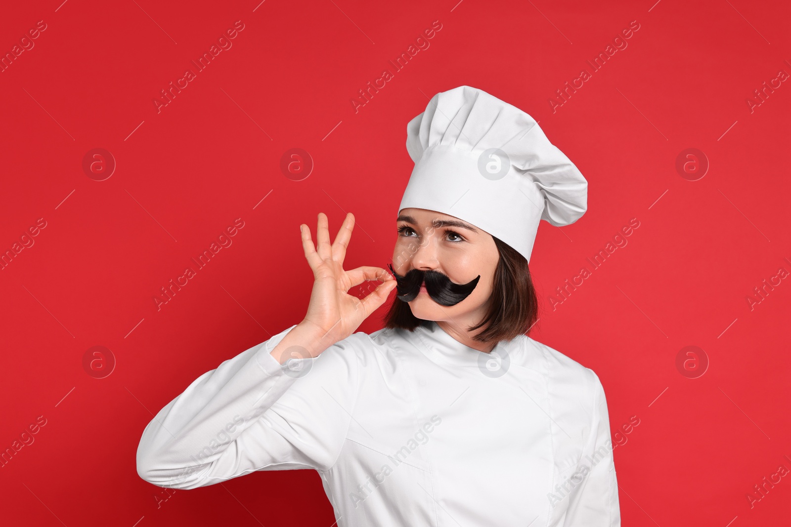 Photo of Confectioner with funny artificial moustache showing ok gesture on red background