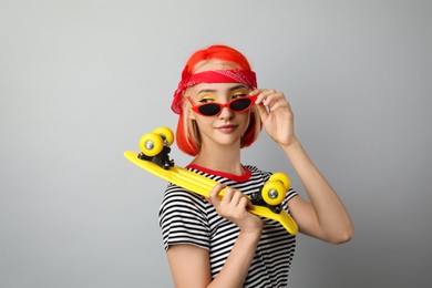 Photo of Beautiful young woman with bright dyed hair holding skateboard on light grey background