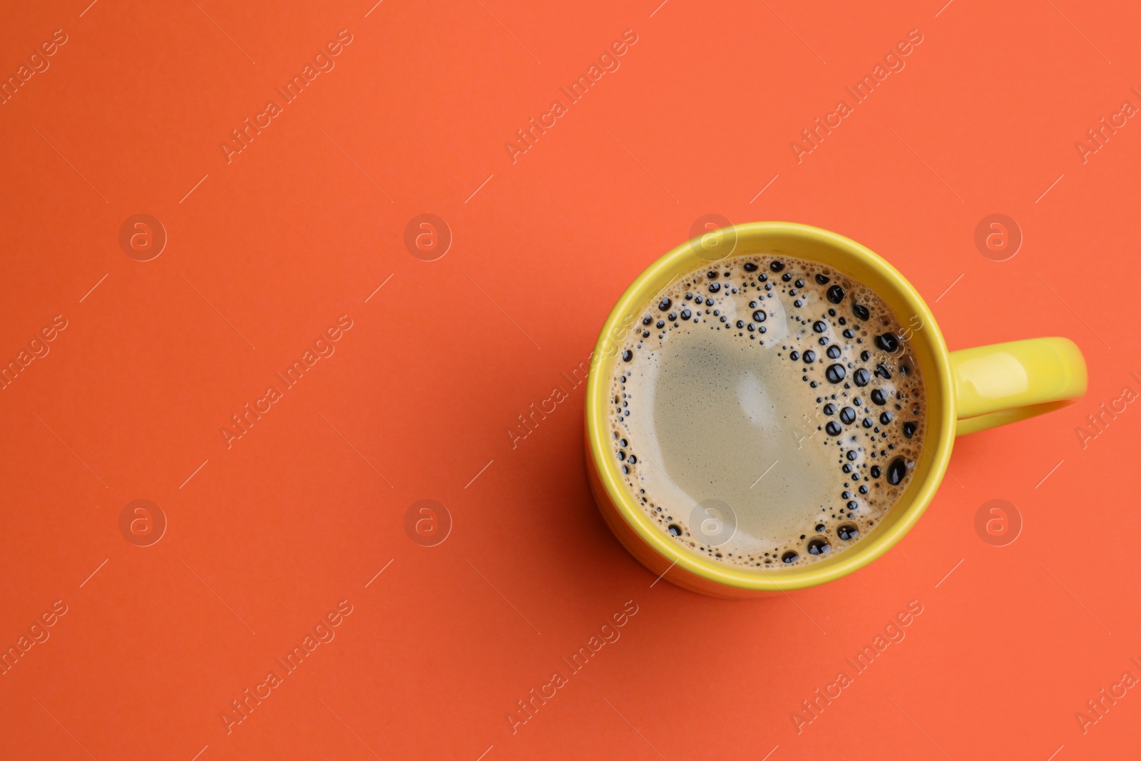 Photo of Yellow mug of freshly brewed hot coffee on orange background, top view. Space for text