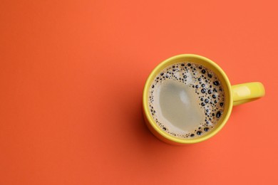 Photo of Yellow mug of freshly brewed hot coffee on orange background, top view. Space for text