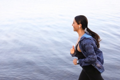 Young sportswoman with wireless earphones running near river