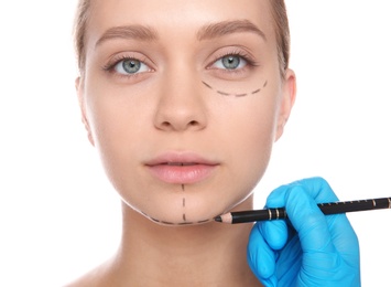 Photo of Doctor marking young woman face before cosmetic surgery on white background