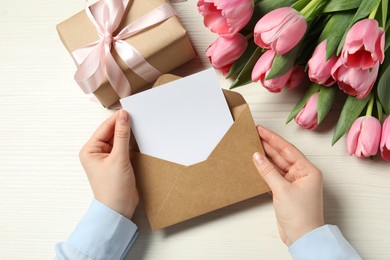 Happy Mother's Day. Woman holding envelope with blank card at white wooden table, top view