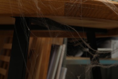 Photo of Old cobweb on wooden table indoors, closeup