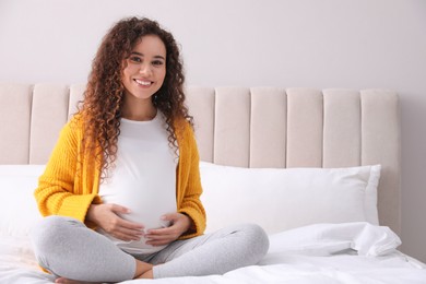 Pregnant young African-American woman sitting on bed at home