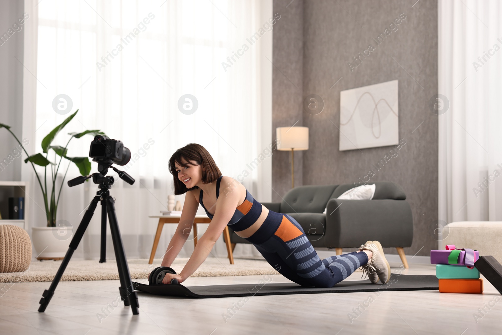 Photo of Happy sports blogger training with ab roller while recording fitness lesson at home