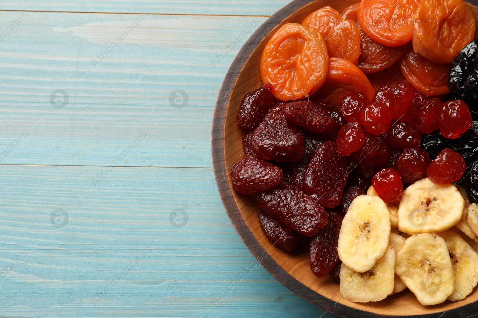 Photo of Mix of delicious dried fruits on light blue wooden table, top view. Space for text