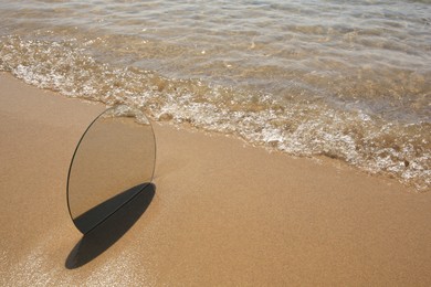 Photo of Round mirror reflecting sea on sandy beach, space for text