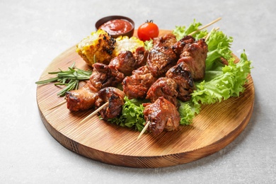 Photo of Wooden board with barbecued meat, garnish and sauce on grey background