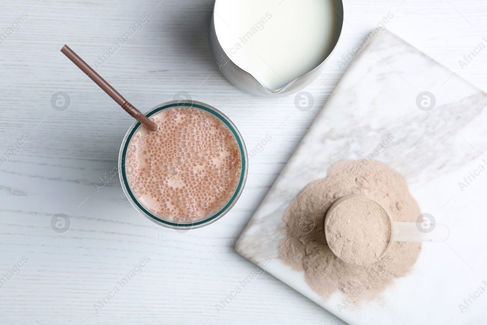 Photo of Glass with protein shake, jug of milk and powder on white wooden table, top view