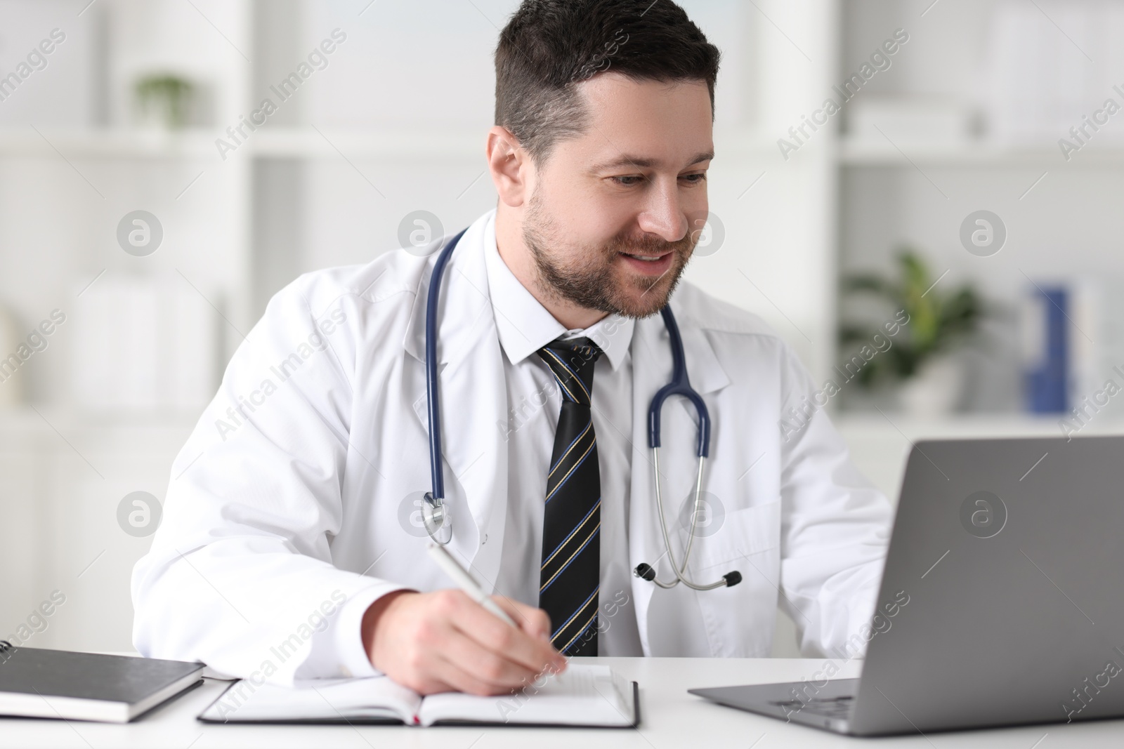 Photo of Doctor having online consultation via laptop at table in clinic