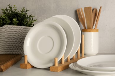 Photo of Set of clean plates and different kitchen utensils on light table near wall