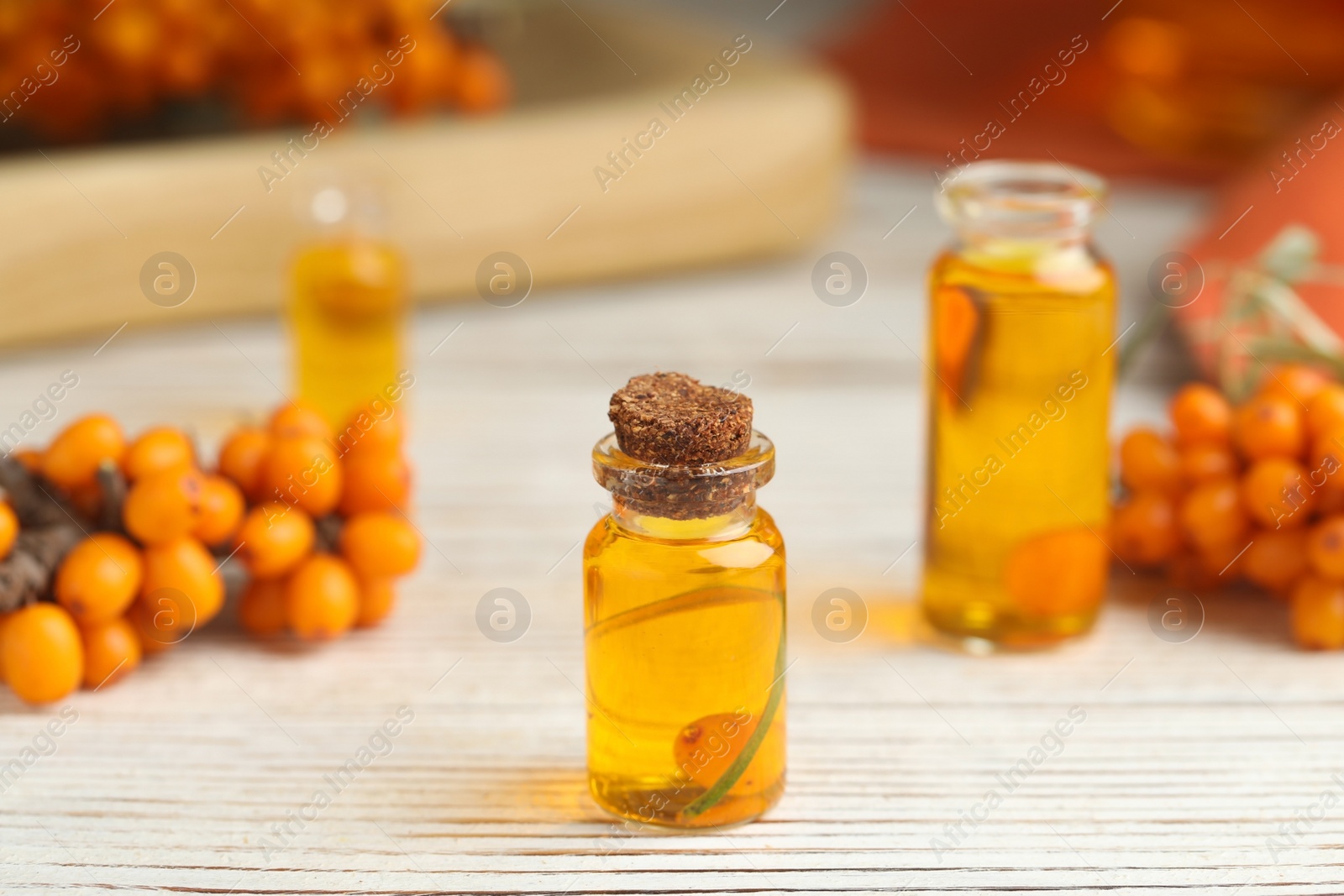 Photo of Natural sea buckthorn oil and fresh berries on white wooden table