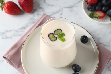Photo of Tasty yogurt in glass and berries on white marble table