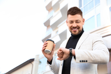 Businessman with cup of coffee on city street in morning