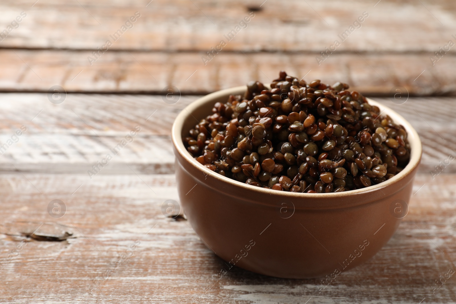 Photo of Delicious lentils in bowl on wooden table, closeup. Space for text