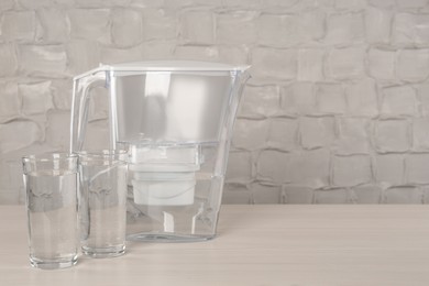 Filter jug and glasses with purified water on white table indoors. Space for text