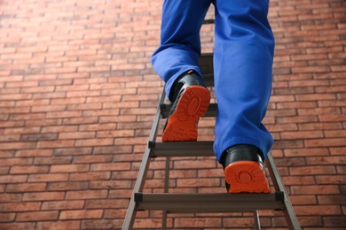 Photo of Professional worker climbing up ladder near brick wall, closeup. Low angle view