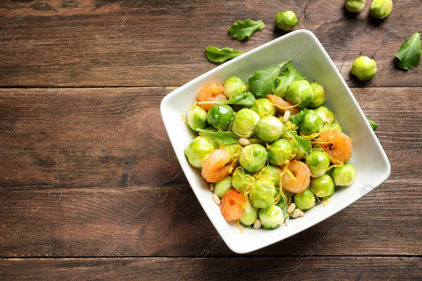 Photo of Bowl of delicious salad with Brussels sprouts and shrimps on wooden table, top view. Space for text