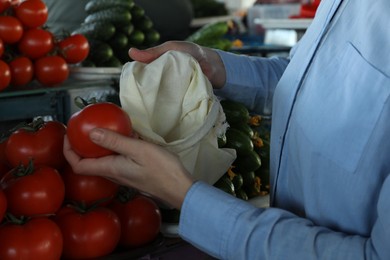 Photo of Woman putting tomato into cotton eco bag at wholesale market, closeup. Life without plastic